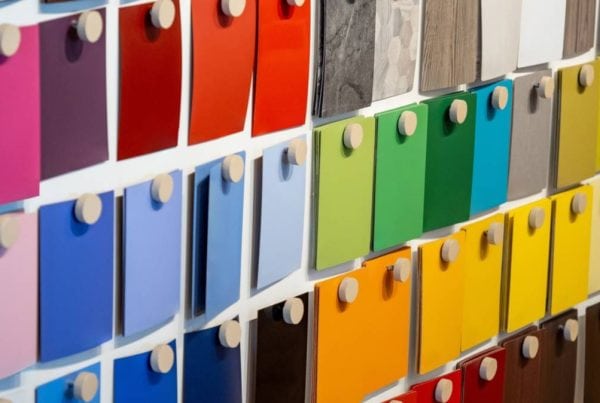 A display wall featuring rows of colorful paint or material samples in various shades, arranged neatly with each sample attached by a round wooden peg.