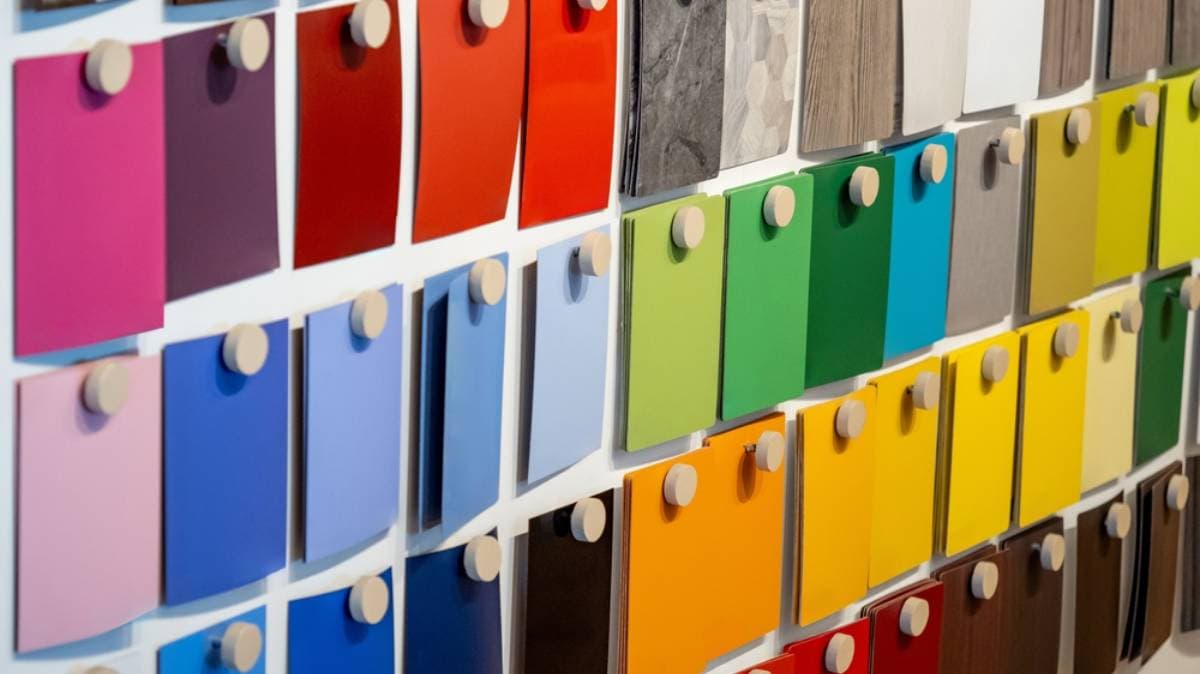 A display wall featuring rows of colorful paint or material samples in various shades, arranged neatly with each sample attached by a round wooden peg.